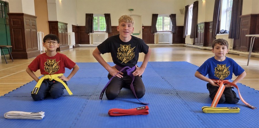 Three Tiger Strike students seated on training mats in their club shirts